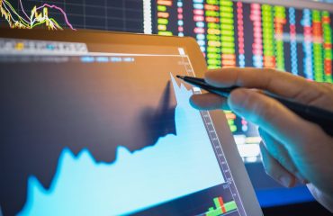 A professional trader using a stylus to interact with a rapidly rising stock chart displayed on a tablet.